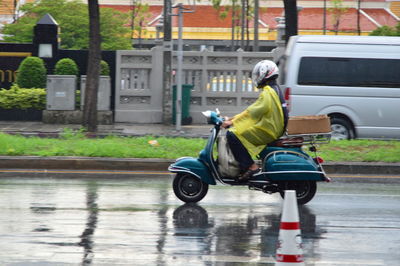 Rear view of man riding motorcycle on street during rainy season