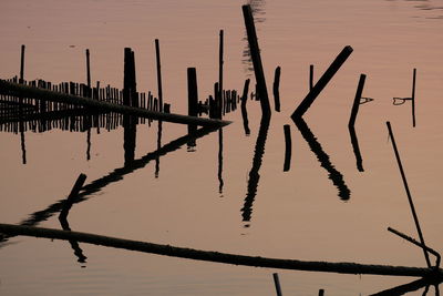 Wooden posts in lake against sky at sunset