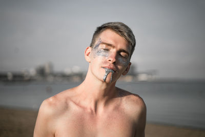 Shirtless man with glitter in mouth and face standing on beach