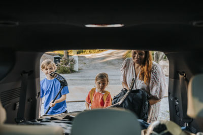 Mother and boys loading ice hockey sticks in car trunk