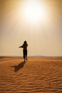 Rear view of woman walking on sand at desert against sky during sunny day