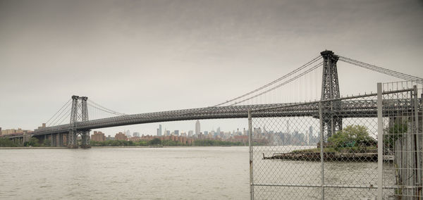 Suspension bridge over river against sky in city