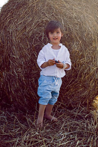 Boy a child in blue pants stands in a mowed field with stacks in the summer