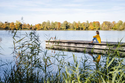 Woman sitting on jetty at lake