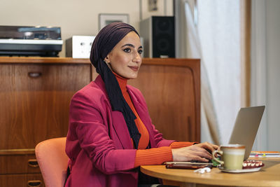 Young woman using laptop while sitting on sofa at home