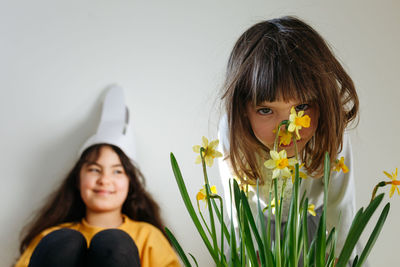 Small girl watching behind  flowers  and bigger girl sitting with easter bunny ears on the head