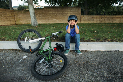 Portrait of boy wearing cycling helmet while sitting on retaining wall by bicycle at park