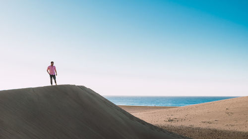 Rear view of man walking on beach against clear blue sky