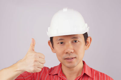 Close-up of male worker wearing hardhat while gesturing against gray background