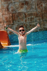 Portrait of shirtless boy with arms raised in swimming pool