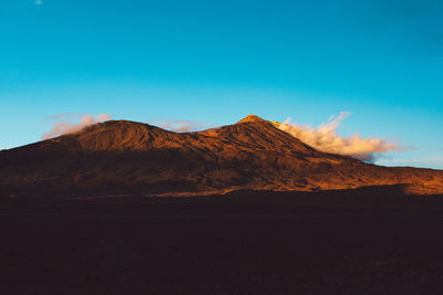 Scenic view of volcanic mountain against blue sky