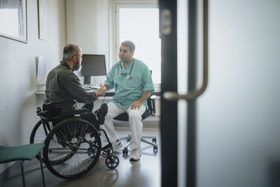 Doctor discussing with male patient sitting in wheelchair at hospital