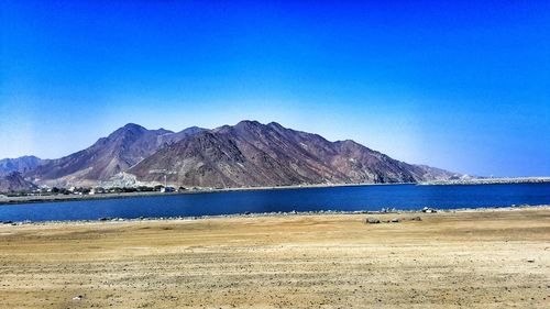 Scenic view of sea and mountains against clear blue sky