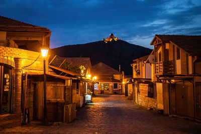 Illuminated street amidst buildings against sky at dusk