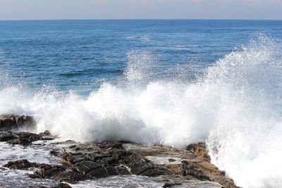 Waves splashing on rocks against sky