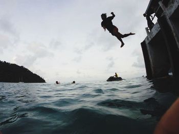 Silhouette people jumping on sea against sky