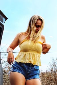 Teenage girl wearing hot pants and yellow top against sky