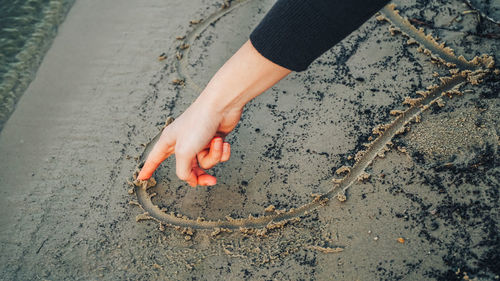 High angle view of hand drawing heart shape on wet sand at beach