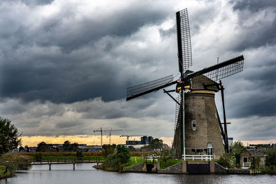 Traditional windmill by river against sky