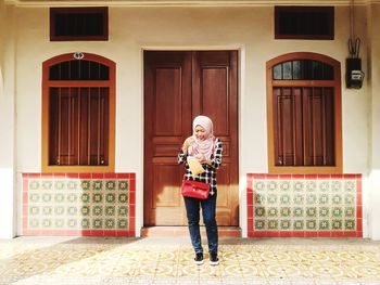 Woman holding plastic bag while standing at entrance of house