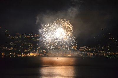 Firework display over illuminated city against sky at night