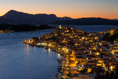 Illuminated city by sea against sky at dusk