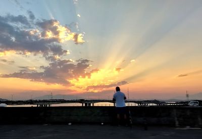 Silhouette man standing on jetty against sea at sunset