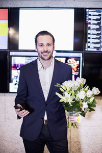 Portrait of successful businessman holding bouquet in office