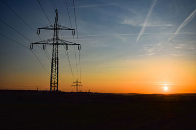 Low angle view of silhouette electricity pylon on field against sky