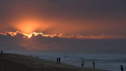 Silhouette people on beach against sky during sunset