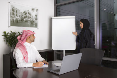 Woman standing by whiteboard looking at man in office