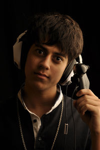 Portrait of teenage boy holding remote control against black background