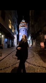 Full length of woman standing on illuminated street in city at night