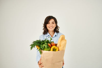 Portrait of smiling young woman holding apple against white background