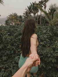 Cropped image of man holding girlfriend hand against plants