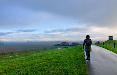 Rear view of man walking on field against sky
