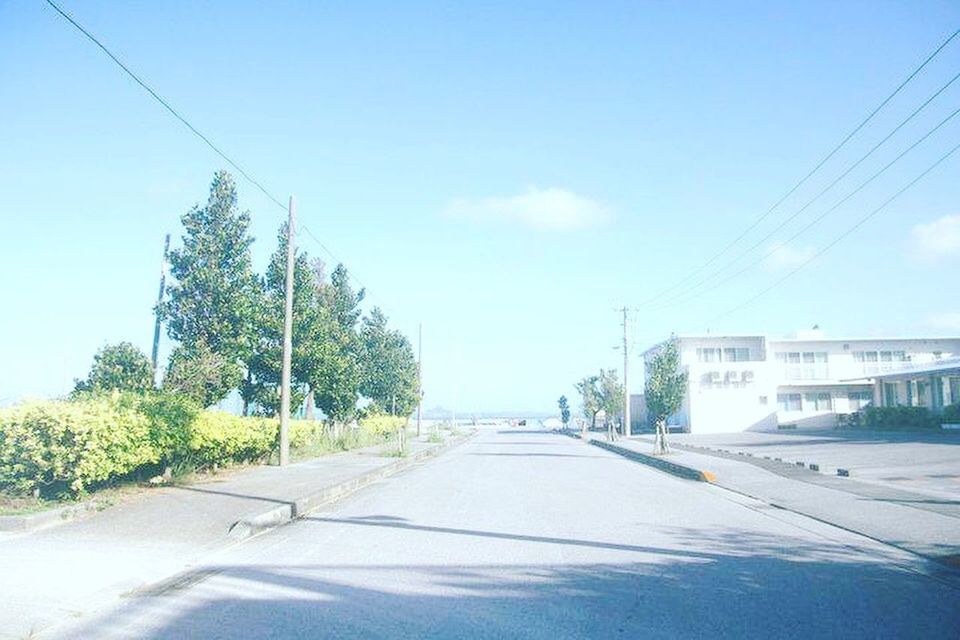 ROAD BY TREES AND CITY AGAINST SKY