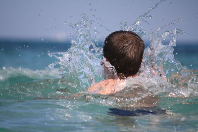 Rear view of boy splashing water at sea