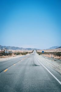 Road leading towards mountain against clear sky