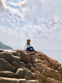 Girl sitting on rock at sea against sky