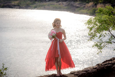 Woman holding umbrella while standing at shore