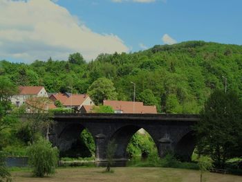 Arch bridge and trees by building against sky