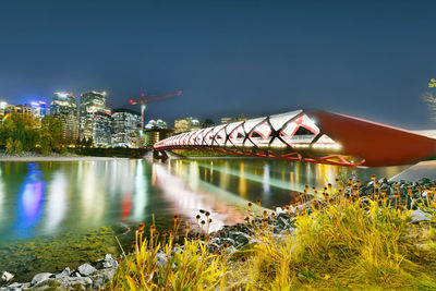 Illuminated buildings by river against sky at night