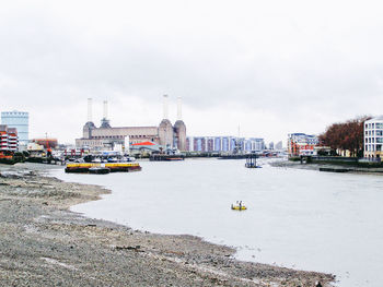 Boats in river by buildings in city against sky