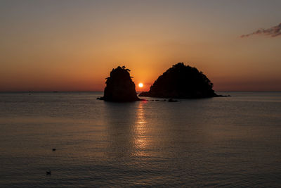 Silhouette rocks in sea against romantic sky at sunset