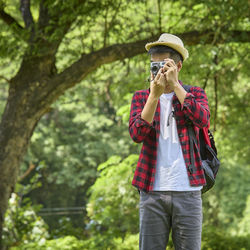 Full length of man holding mobile phone while standing against trees