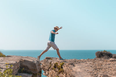 Rear view of woman standing on rock against clear sky