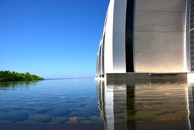 Swimming pool by lake against clear blue sky