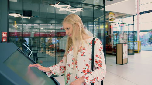 Beautiful woman touching digital screen while standing in shopping mall