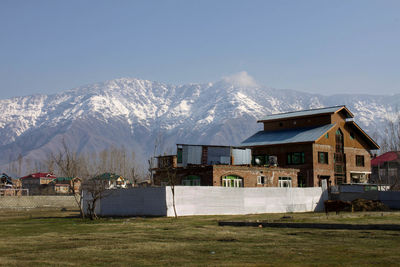 Houses on field by snowcapped mountains against sky